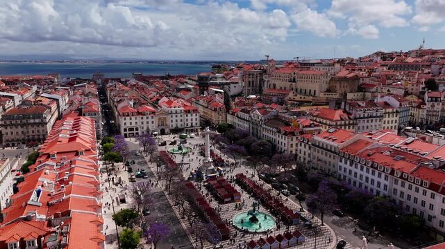 Aerial orbit of Rossio Square and downtown Lisbon with jacaranda trees and Tagus River in Portugal