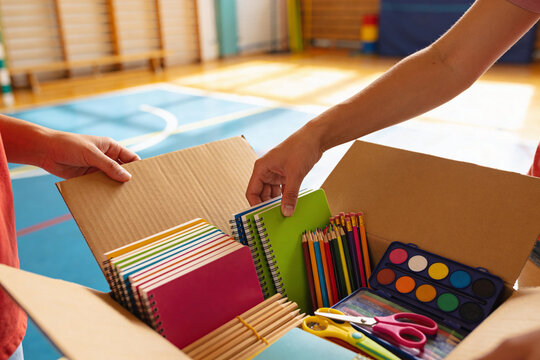 Hands packing school supplies into a donation box in a gymnasium