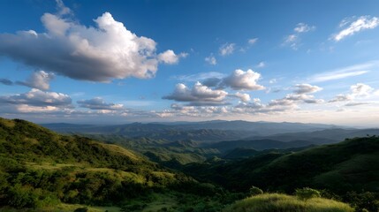 Fototapeta premium An expansive view of rolling green hills and mountains under a bright cloudy blue sky