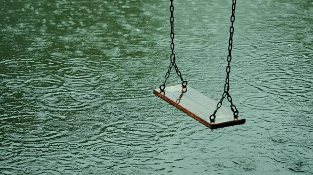 Empty wooden swing board hanging over rippling green water surface in the rain