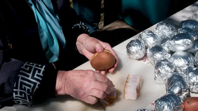 cut the potatoes with a knife, stuff with lard, wrap in foil and bake, baked potatoes on the fire with lard, delicious food in the village. High quality 4k footage