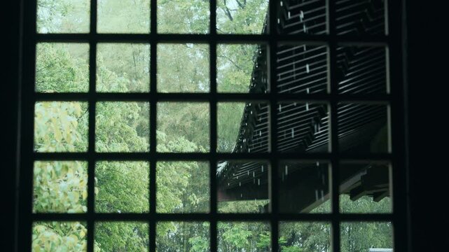 View of traditional building roof and green trees through a Chinese lattice window frame