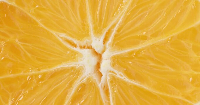 Macro top view close-up shot of fresh round orange slice rotating slowly. The vibrant orange citrus fruit slice spins smoothly, showcasing its juicy pulp segments