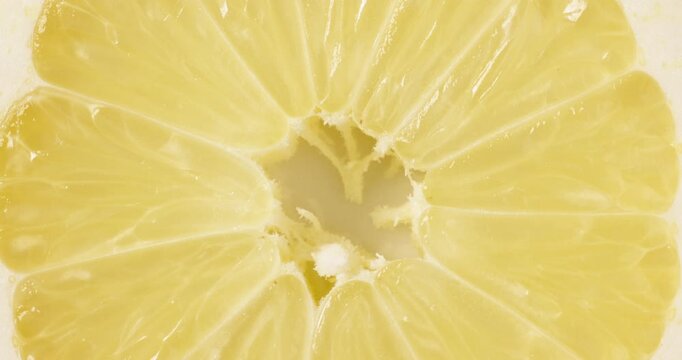 Macro top view close-up shot of a fresh round lemon slice rotating slowly. The vibrant yellow citrus fruit slice spins smoothly, showcasing its juicy pulp, detailed texture, and natural patterns