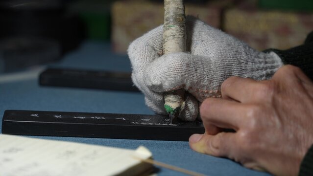 Craftsman wearing gloves holding a carving knife to carve a long wooden block