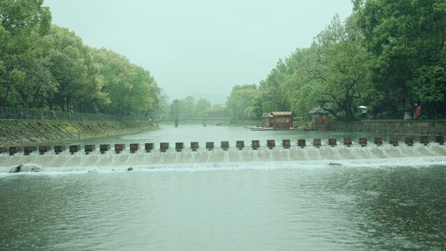 Misty view of the Su Causeway weir in Hangzhou West Lake with lush green trees and flowing water
