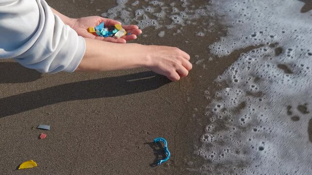 Volunteer collecting microplastic waste on a polluted sandy beach. Female volunteer hands collecting dangerous plastic and microplastic garbage from the sand on a beach