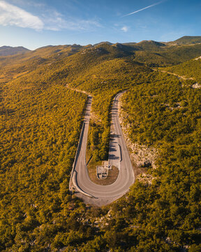 Aerial view of a winding mountain road with a sharp hairpin turn surrounded by lush green hills and rocky peaks under a clear blue sky Rijeka, Primorje-Gorski Kotar, Croatia.