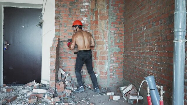 Builder removing brick wall with power tool during interior renovation. Concept of home improvement and demolition work.