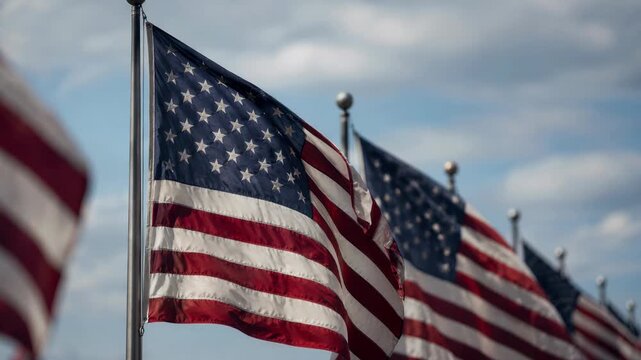 Multiple American flags waving in the breeze against a cloudy sky. A row of United States national banners flying on poles with shallow depth of field. Patriotic USA holiday concept