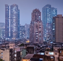 Fototapeta premium Macau, China : dense residential highrises and aging apartment buildings glowing through humid night haze in the urban skyline of Macau.