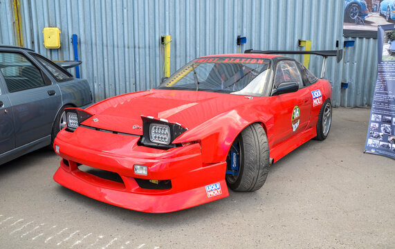 Bright red Nissan 200SX (S13) drift car featuring a widebody kit, large rear wing, and pop-up LED headlights is a staple of global car culture and high performance tuning