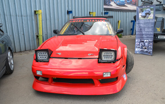 Bright red Nissan 200SX (S13) drift car featuring a widebody kit, large rear wing, and pop-up LED headlights is a staple of global car culture and high performance tuning