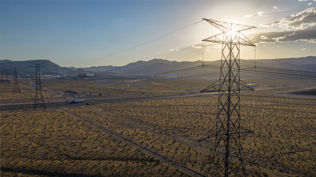 Aerial view of high-voltage power lines and transmission towers stretching across a desert landscape with mountains in the background Enterprise, Nevada, United States.
