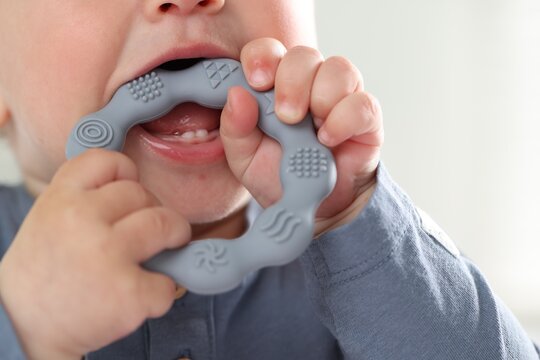 First baby teeth. Cute child with teether at home, closeup