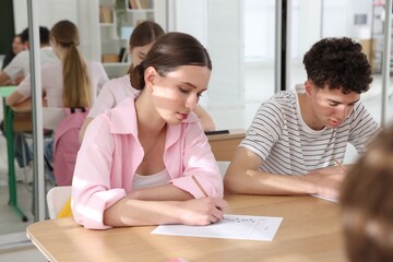 Fototapeta premium Group of students taking test at wooden desks in classroom