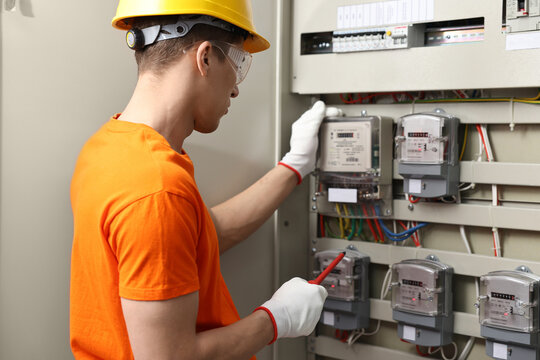 Electrician with screwdriver checking electrical meter indoors