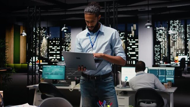 Portrait of middle eastern staff walking with laptop in the office at night, busy planning goals and solving assignment for company development. Man professional making an action plan.