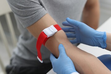 Fototapeta na wymiar Nurse putting medical tourniquet on patient's arm in clinic, closeup