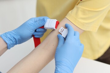 Fototapeta na wymiar Nurse putting medical tourniquet on patient's arm in clinic, closeup
