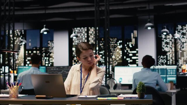 Female accountant in office using laptop, writing down information, working overtime to finish paperwork before deadline. Woman transcribing from device, doing note taking, documenting research.