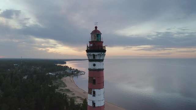Orbital aerial footage of Osinovetsky lighthouse on the shore of Ladoga lake on summer sunset. Ladozhskoye Osero village, Leningrad Oblast, Russia.