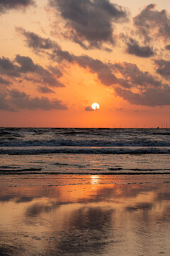 View of Strand Wijk aan Zee at sunset with orange clouds reflecting on the wet sand and waves crashing on the shore in Wijk aan Zee, North Holland, Netherlands.