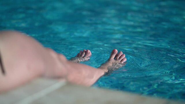 Woman relaxing with foot is in pool water, slow motion. The water is clear and calm. The person is laying in the water with their foot in it.