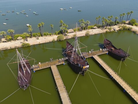 Several historic sailing ships in a water basin surrounded by tropical palm trees under a clear sky, aerial view, Muelle de las Carabelas, reproductions of La Ni&ntilde;a, La Pinta and La Santa Mar&iacute;a, Museum, Palos de la Frontera, Province of Huelva, Andalusia, Spain
