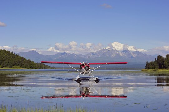Seaplane Beaver de Havilland lands on a lake off snow-covered mountain Denali, Alaska, USA