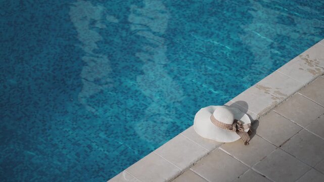 A white hat is sitting on the edge of a luxury hotel swimming pool with blue tiles