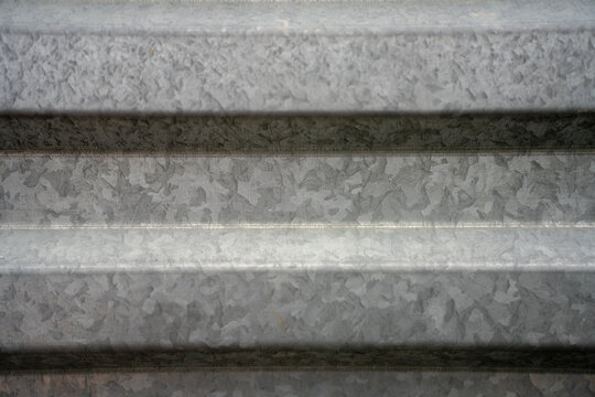 Close up background texture of corrugated galvanized steel sheet, showing grey metallic zinc coating pattern with horizontal lines and spangle crystallization.
