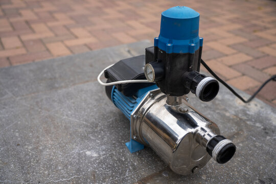 Electric water pressure booster pump with automatic electronic controller unit installed on top, detail of domestic or garden water supply system equipment on concrete ground.