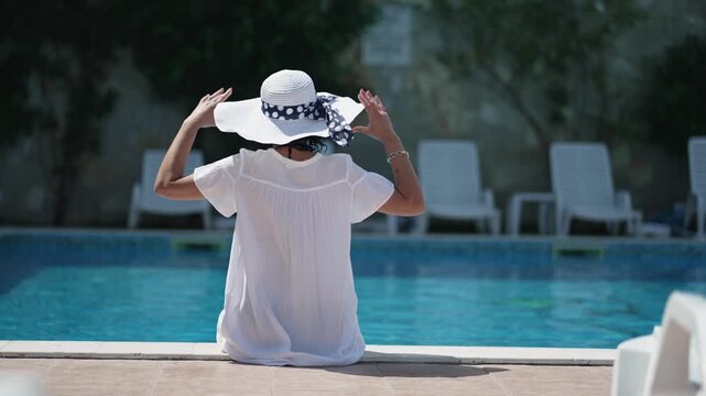 A woman sitting in a pool, wearing a white hat and a black and white polka dot scarf