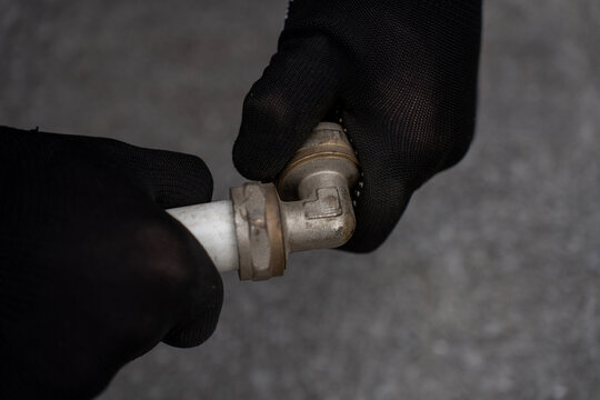 Close up of hands in black protective gloves assembling or twisting a metal brass elbow fitting connected to a white pex composite pipe.