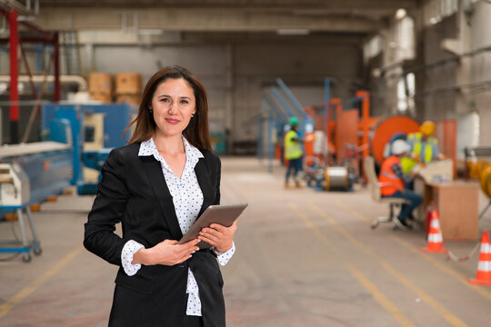 Businesswoman holding tablet on factory floor with workers in background