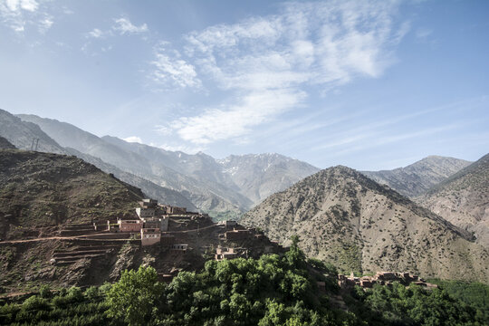 View of the traditional Berber village of Tizi Oussem nestled on a hillside with rugged Atlas Mountains and lush greenery under a blue sky Tizi Oussem, Marrakech-Safi, Morocco.