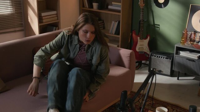 High angle shot of young adult female music producer rising from sofa having creative spark then playing music on MIDI keyboard connected to laptop at home recording setup