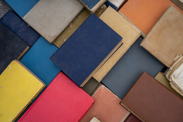 Fototapeta premium Top view flat lay of vintage secondhand books with worn colorful covers arranged tightly together, forming a textured background of old literature.
