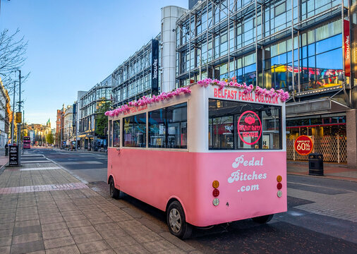 Belfast, UK, April 24, 2026. The street view of a vibrant pink Belfast Pedal Pub mobile bar vehicle at Royal Avenue on a sunny day.