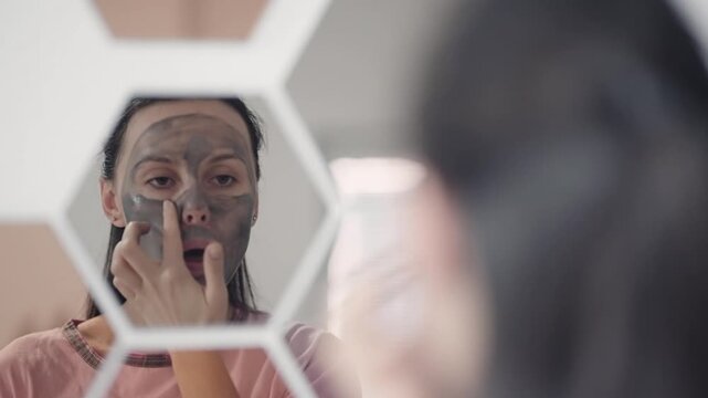 Young Woman Applying Face Mask in Mirror for Self Care Routine