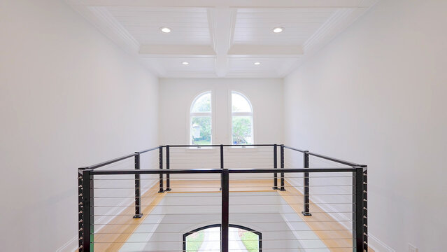 Modern house interior featuring a white hallway loft balcony with black metal cable railings and coffered ceiling lights