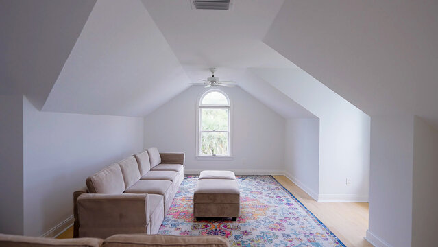 Cozy attic living room with a long beige sectional sofa, colorful patterned rug, and a central arched window