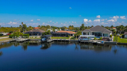 Fototapeta premium Scenic drone shot of luxury waterfront suburban houses with private boat docks and swimming pools along a calm canal waterway under a bright blue sky