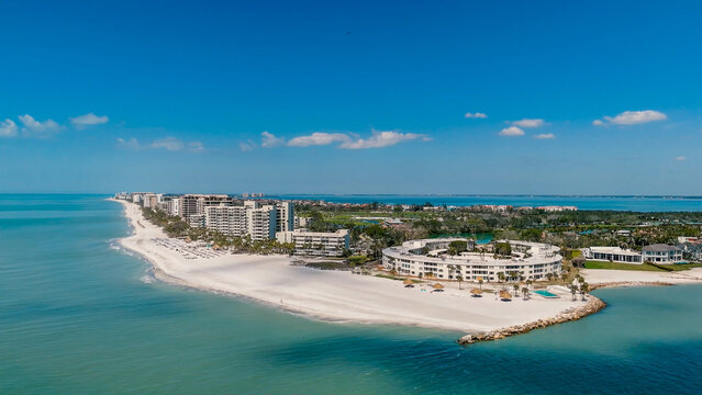 Aerial view of a beautiful white sand beach resort with luxury high-rise condominium buildings next to the turquoise ocean water under a clear blue sky