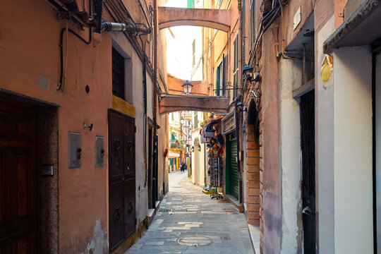 A narrow alley with stone arch bridges lined with shops, cafes, and apartments in the historic center of Sanremo, Italy, in the Ligurian region.
