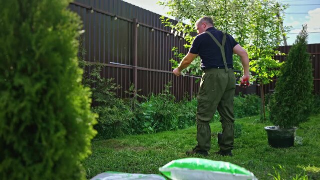 Professional gardener in uniform preparing the backyard for landscaping by stretching a marking string across the green lawn, setting up the area for planting or construction work
