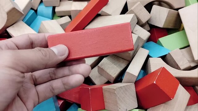 Close-up image of a boy's hand holding a wooden block for creativity and self-development while enjoying free time. Skills through puzzle activities and creativity in table games at home.