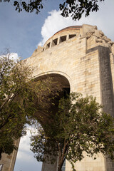 Fototapeta premium Set against a bright sky with surrounding trees, this iconic landmark in Mexico City reflects historical significance, cultural heritage, and the grandeur of large-scale urban monuments.