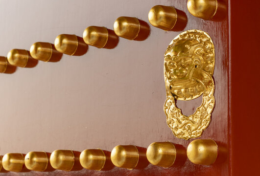 View of traditional red lacquered door with golden studs and an ornate lion head door knocker at the Forbidden City in Beijing, Beijing, China.